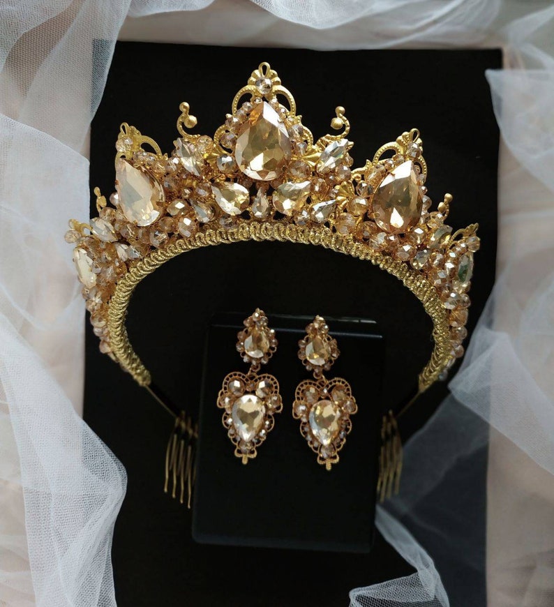 Puede incluir: Una tiara dorada con una corona en forma de l&aacute;grima y pendientes a juego. La tiara est&aacute; adornada con diamantes de imitaci&oacute;n transparentes y color champ&aacute;n.
