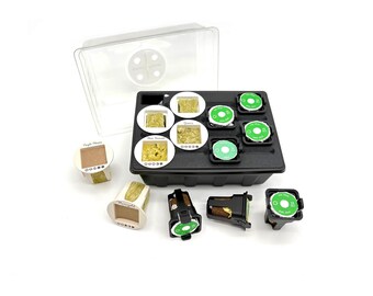 Peut inclure: Un plateau de germination intérieur en plastique noir avec un couvercle transparent, comprenant plusieurs emplacements circulaires. Certains contiennent des éponges de culture brun clair, d'autres des étiquettes vertes avec du texte blanc.
