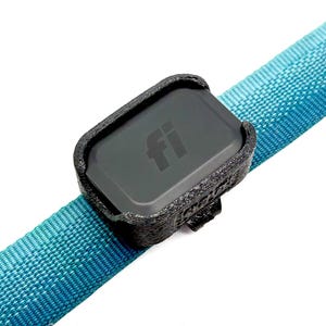 May include: A black rectangular electronic tracking device with the letters fi printed on the front, secured within a textured black 3D-printed plastic holder attached to a bright turquoise woven fabric strap that runs diagonally across the frame.