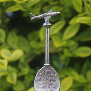 May include: A silver spoon with a miniature aeroplane on top. The spoon has the text "15th September 1940-1985 45th Anniversary Battle" engraved on the bowl.