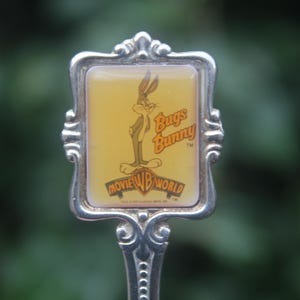 May include: Silver-toned spoon featuring a Bugs Bunny image. The rectangular center has a yellow background with Bugs Bunny standing, the words "Bugs Bunny" and "Movie WB World" are also visible.