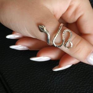 Op de afbeelding: Een zilveren slangenring met een textuur. De ring wordt gedragen op een vinger met witte nagellak.