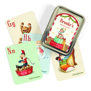 May include: A set of colorful alphabet matching cards in a silver tin. The cards feature illustrations of Christmas-themed objects like a gingerbread man, a nutcracker, and a xylophone. The tin has the title "Brooke's Matching Game" and the text "My Very Own Christmas".