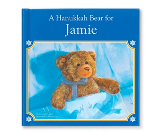 May include: A blue book with a gold border and a picture of a brown teddy bear in a blue bed. The title of the book is "A Hanukkah Bear for Jamie".