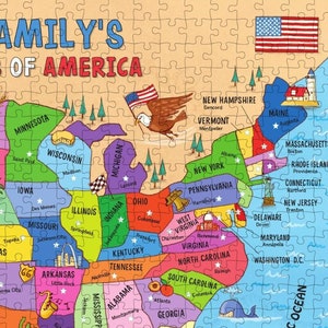 May include: A colorful map of the United States with each state outlined and labeled. The map features a cartoon eagle holding the American flag, and each state has a small star and a city name. The map is on a light brown background.