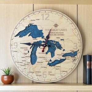May include: Wooden wall clock featuring a map of the Great Lakes, including Superior, Michigan, Huron, Erie, and Ontario. The clock has blue water details, black hands, and red second hand. The clock is approximately 12 inches in diameter.