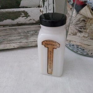 May include: A white glass jar with a black lid and a brown label that reads "PURIFIED PAPRIKA GRIFFITH'S".