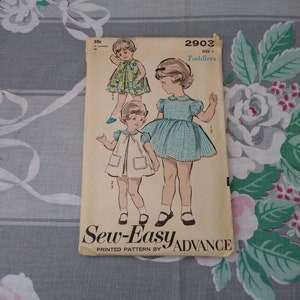 May include: Sew-Easy Advance pattern 2903 for toddlers, featuring two girls wearing dresses. The pattern is printed on a white background with blue text. The price is 50 cents.