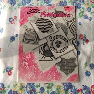 May include: A vintage "Star Potholders" booklet with a pink cover featuring illustrations of various potholder designs, including a fish, crab, and seashell. The booklet is lying on a floral patterned tablecloth.