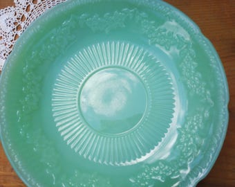 May include: A vintage green glass plate with a scalloped edge and a floral design. The plate has a raised center with a fluted design.