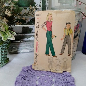 May include: Vintage Simplicity sewing pattern number 2003, size 8, for a girl's outfit. The pattern is printed on a white background with a green and white plaid fabric design. The pattern includes a shirt, pants, and a vest. The pattern is priced at 25 cents.