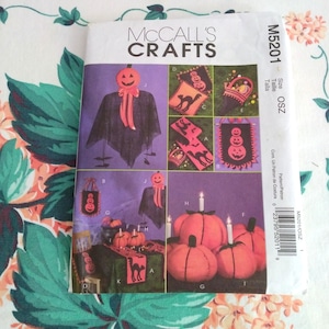 May include: A McCall's Crafts pattern envelope featuring Halloween-themed craft projects. The designs include pumpkin-headed figures, banners, and pumpkin decorations. The color palette includes orange, black, and purple.
