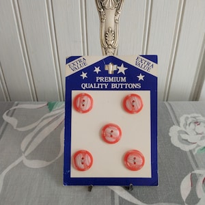 May include: A card of five red and white premium quality buttons. The card has blue borders and the text "EXTRA VALUE" and "PREMIUM QUALITY BUTTONS". The card is held up by a decorative silver spoon.