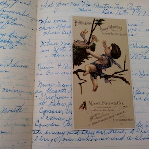 May include: A vintage advertisement for Buckeye Lawn Mowers, featuring a child sitting on a branch with two birds. The advertisement is printed on a cream-colored card with black text. The text reads "Buckeye Lawn Mowers, Imitated but not equaled. Mast, Foos & Co., Manufacturers of Iron Turbine Wind Engines, Force Pumps, Iron Fencing &c. Buckeye Lawn Mowers, Springfield, Ohio."