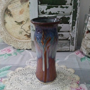May include: A tall, ceramic vase with a purple, blue, and brown glaze. The vase has a unique, abstract design with a white stripe running down the center.