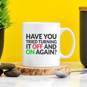 May include: White ceramic mug with black text that reads "Have you tried turning it off and on again?" The words "off" and "on" are in red and green, respectively.
