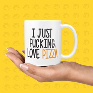 May include: White ceramic coffee mug with a black and orange design. The mug has a handle and says "I JUST FUCKING LOVE PIZZA" with a heart symbol.