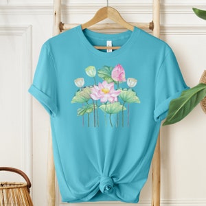 May include: A turquoise blue t-shirt with a watercolor design of pink and white lotus flowers with green leaves.