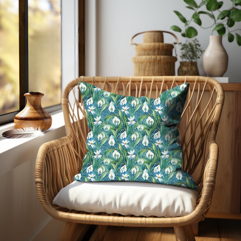 This pillow features a repeating pattern of Art Nouveau white snow drop flowers nestled among green leaves on a blue background in a lovely Victorian style botanical print. Reminiscent of William Morris Art Nouveau style.