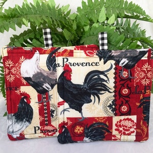 May include: Two red and white quilted pot holders with a rooster and floral pattern. The larger pot holder has the text "La Provence" on it.