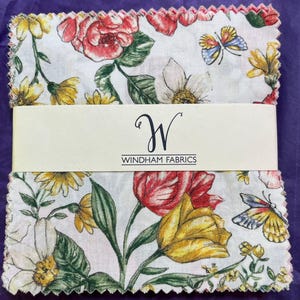 May include: A stack of square fabric swatches with pinked edges, featuring a floral pattern with red and yellow tulips, white daisies, and butterflies on a white background. A cream-colored paper band wraps the center with the text Windham Fabrics.