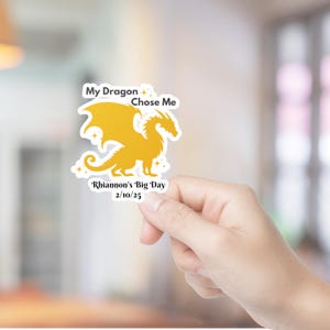 May include: A yellow dragon silhouette with stars and the text "My Dragon Chose Me" and "Rhiannon's Big Day 2/10/25".