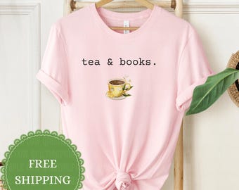 Puede incluir: Una camiseta de manga corta de color rosa claro con el texto negro "tea & books." centrado sobre una pequeña ilustración en acuarela de una taza de té amarilla llena de té, adornada con una rodaja de limón y hojas verdes sobre un platillo.