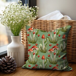 Lovely square accent or throw pillow with a repeating pattern of a group of red capped mushrooms with white stems with green grass and leaves on a sage green background. Printed on both sides.