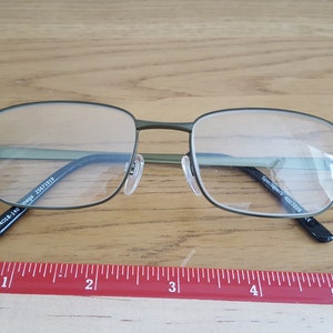 Op de afbeelding: Groene metalen bril met een montuur en heldere glazen. De pootjes van de bril zijn gemarkeerd met "SpecSAVERS 400.1228" en "54018-140 mega 25671919".