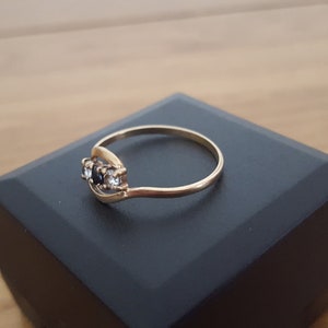 May include: A gold ring with three stones, two black and one white, set in a curved band.
