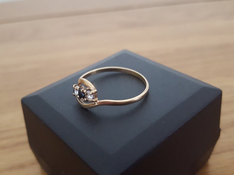 May include: A gold ring with three stones, two black and one white, set in a curved band.