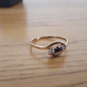 May include: A gold ring with a black gemstone and smaller white gemstones set in a curved band.