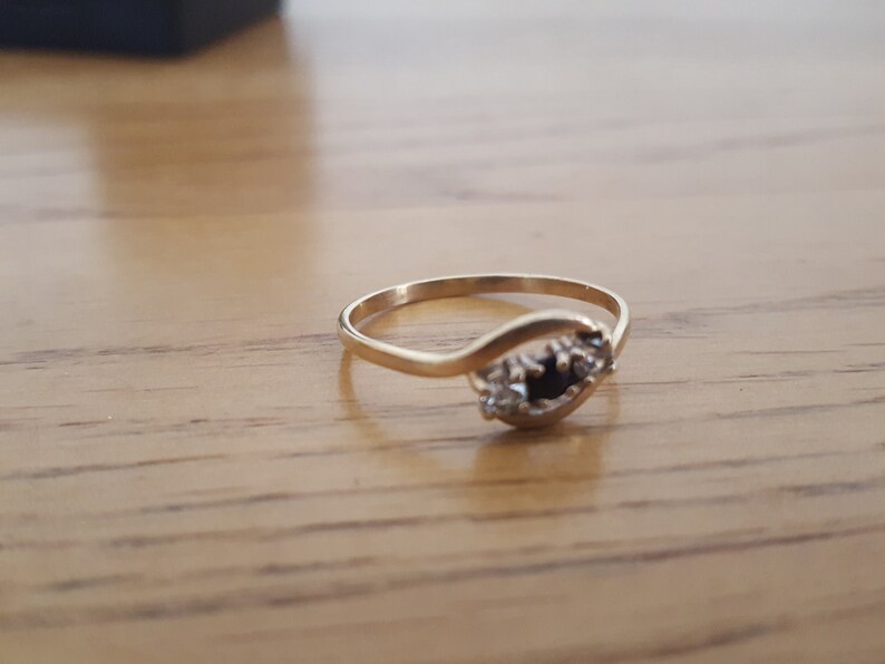 May include: A gold ring with a black gemstone and smaller white gemstones set in a curved band.