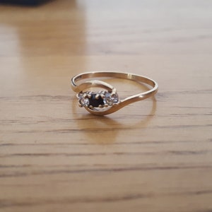 May include: A gold ring with a black stone and two smaller white stones set in a curved band.