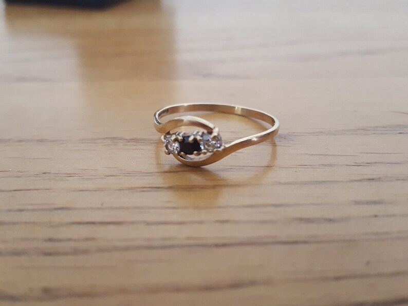 May include: A gold ring with a black stone and two smaller white stones set in a curved band.