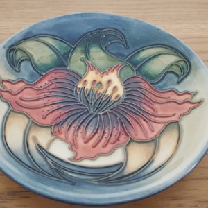 Puede incluir: Un plato de cerámica azul y blanco con un diseño floral. La flor es roja, amarilla y verde. El plato es una pieza decorativa.