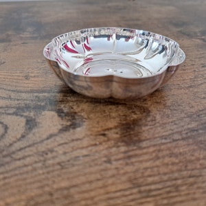 May include: A silver bowl with a scalloped edge. The bowl is empty and sitting on a wooden surface.