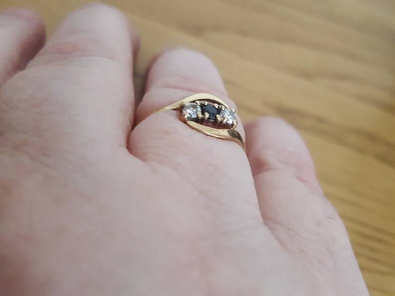 May include: A gold ring with three stones. The center stone is black and the two stones on either side are white.