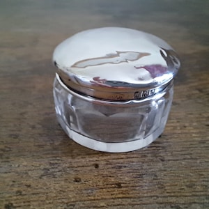 Könnte beinhalten: Eine gläserne Dose mit einem silbernen Deckel und einem geschliffenen Glasdesign. Der Deckel hat eine Punze auf der Unterseite.