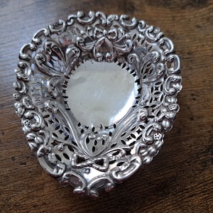 Pode incluir: Um prato de filigrana de prata com um delicado desenho floral. O prato é oval e tem uma borda elevada.