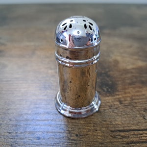 May include: A silver sugar shaker with a perforated top and a smooth, cylindrical body.