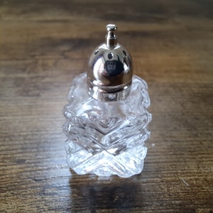 Op de afbeelding: Een glazen zoutvaatje met een zilveren deksel en een getextureerd ontwerp.