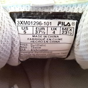 以下が含まれることがあります： Filaの靴のラベルのクローズアップ。ラベルには、サイズがUS 5、EUR 37 1/2、UK 4、MEX 23 1/2と表示されています。ラベルには、靴が中国製であることも記載されています。アッパーは合成繊維、裏地はテキスタイル、ソールはEVA/ラバーです。