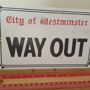 Może przedstawiać: Biały metalowy znak z czarnym napisem "WAY OUT" i czerwonym napisem "City of Westminster".
