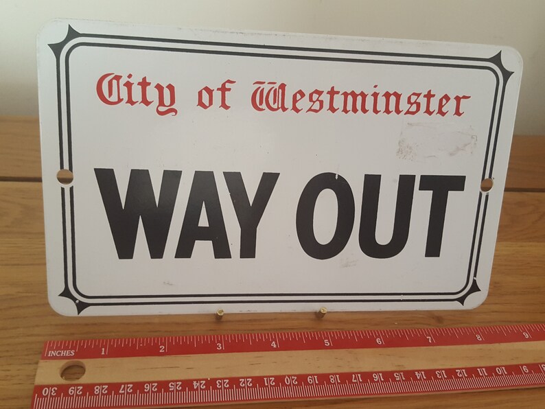 Może przedstawiać: Biały metalowy znak z czarnym napisem "WAY OUT" i czerwonym napisem "City of Westminster".