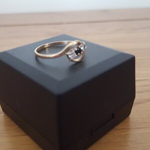 May include: A gold ring with a black and white stone setting. The ring is in a black ring box.