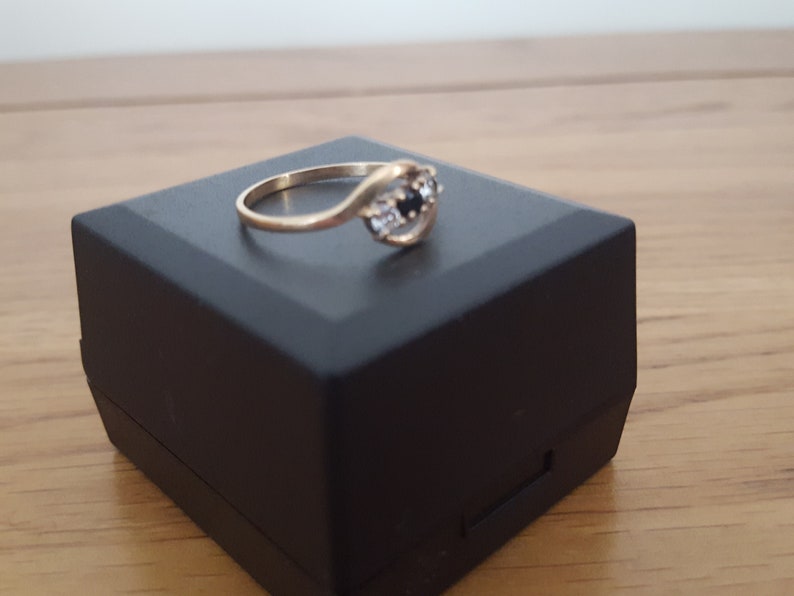 May include: A gold ring with a black and white stone setting. The ring is in a black ring box.