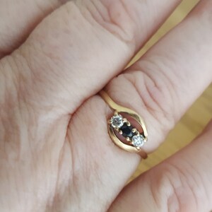 May include: A gold ring with three stones. The center stone is black, and the two stones on either side are white.