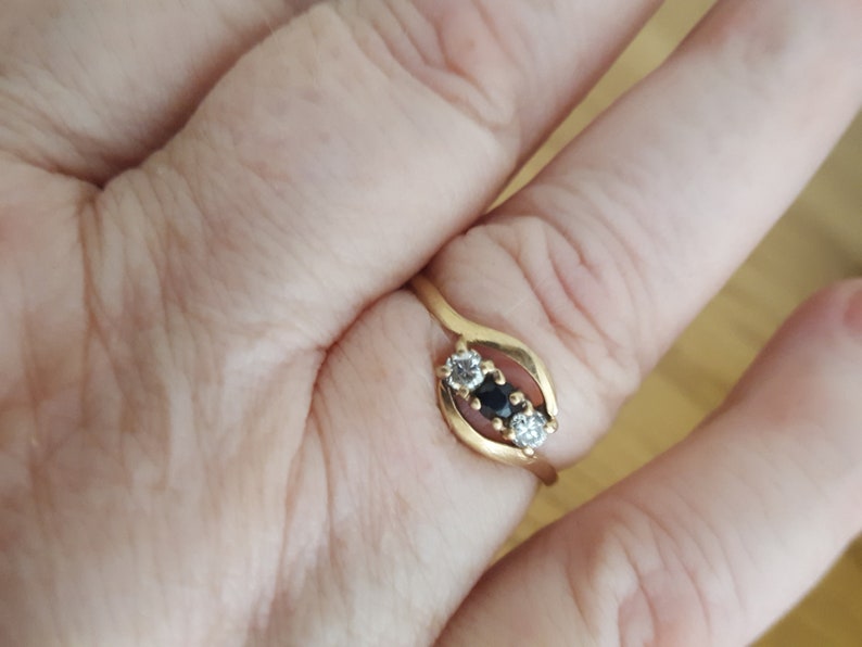 May include: A gold ring with three stones. The center stone is black, and the two stones on either side are white.