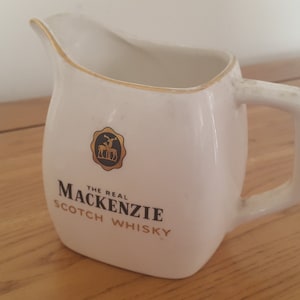 May include: White ceramic pitcher with a gold rim and a black and gold logo that reads "The Real Mackenzie Scotch Whisky".